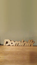 Sample design: freestanding laser-cut wooden name sign spelling Dominik, standing on a wooden shelf